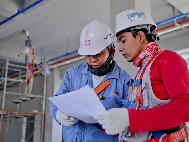 Two industrial workers in hard hats reviewing plans on site