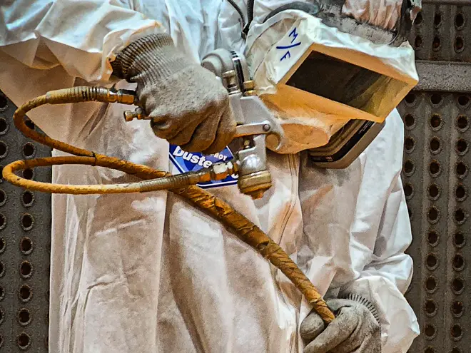Sandblaster in full protective gear preparing a steel surface